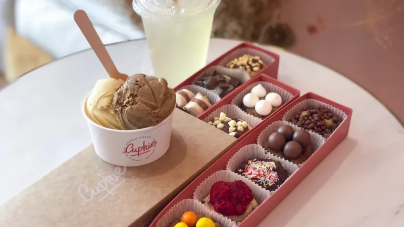 Coffrets rouges de bouchées de cookie dough garnies, à côté d’une cup de glace Cupkie et d’une citronnade