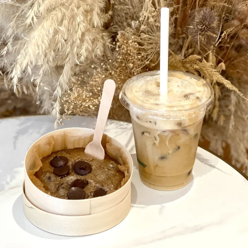 Un hot cookie aux pépites de chocolat dans sa boîte, à côté d’un iced latte
