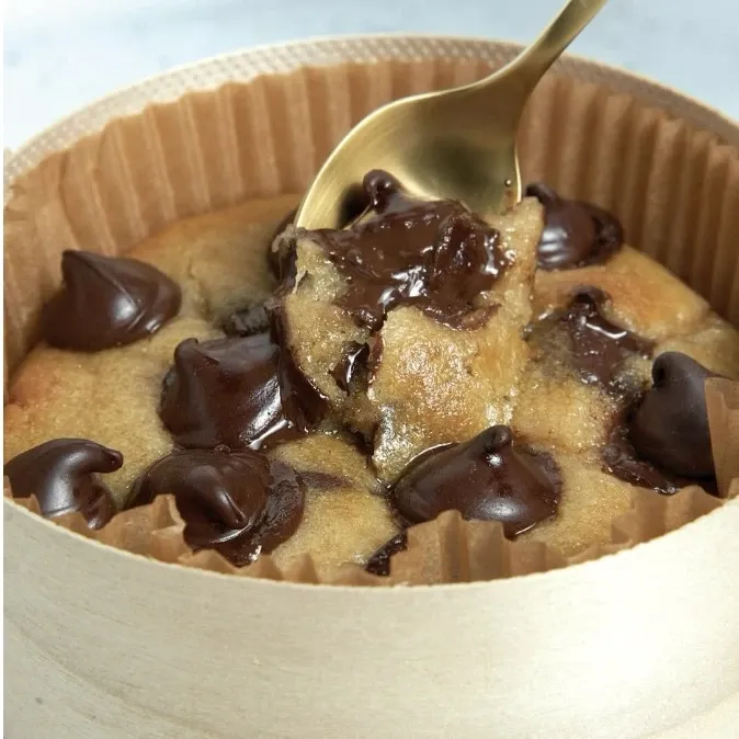 Hot cookie coulant aux pépites de chocolat dans sa boîte, une cuillère dorée plongée dedans